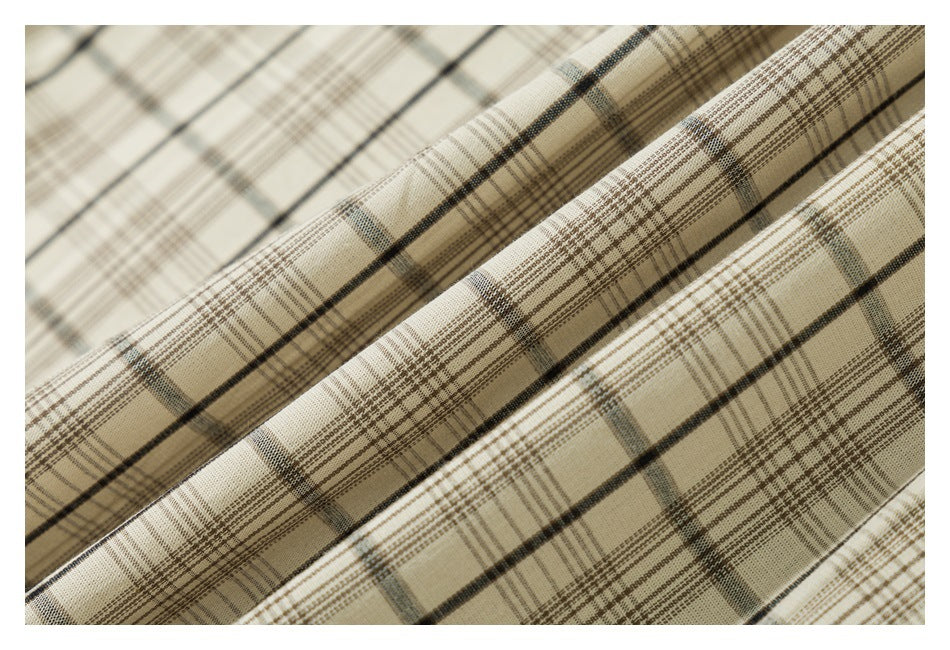 Macro view of folded cream plaid fabric with intersecting brown, charcoal, and muted gray lines.