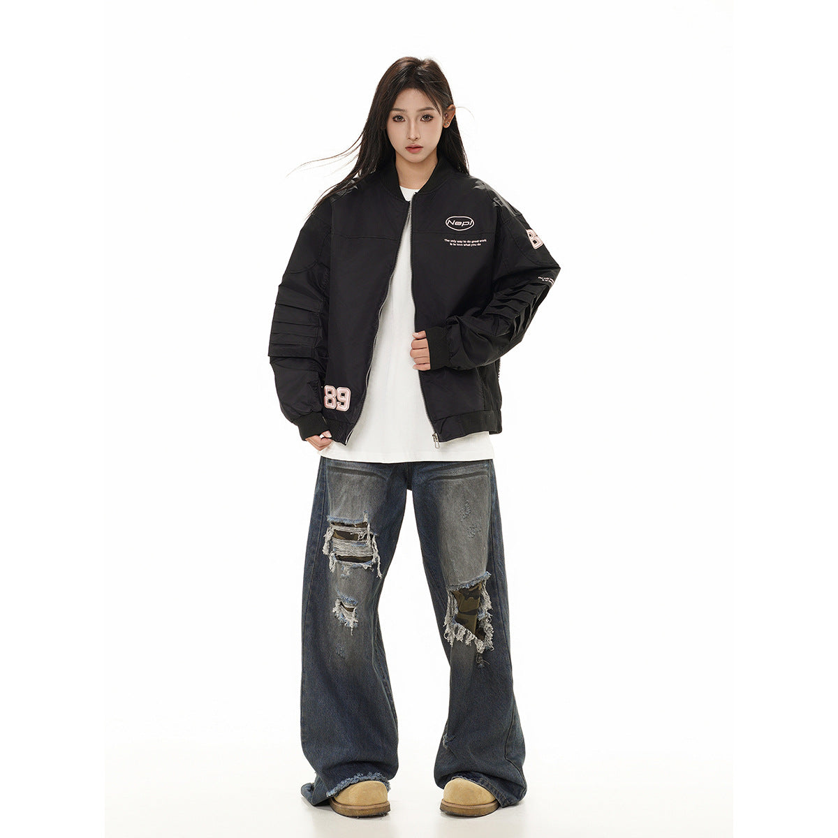 Front view of a model in a black graphic bomber jacket, white shirt, distressed wide-leg jeans and tan shoes.