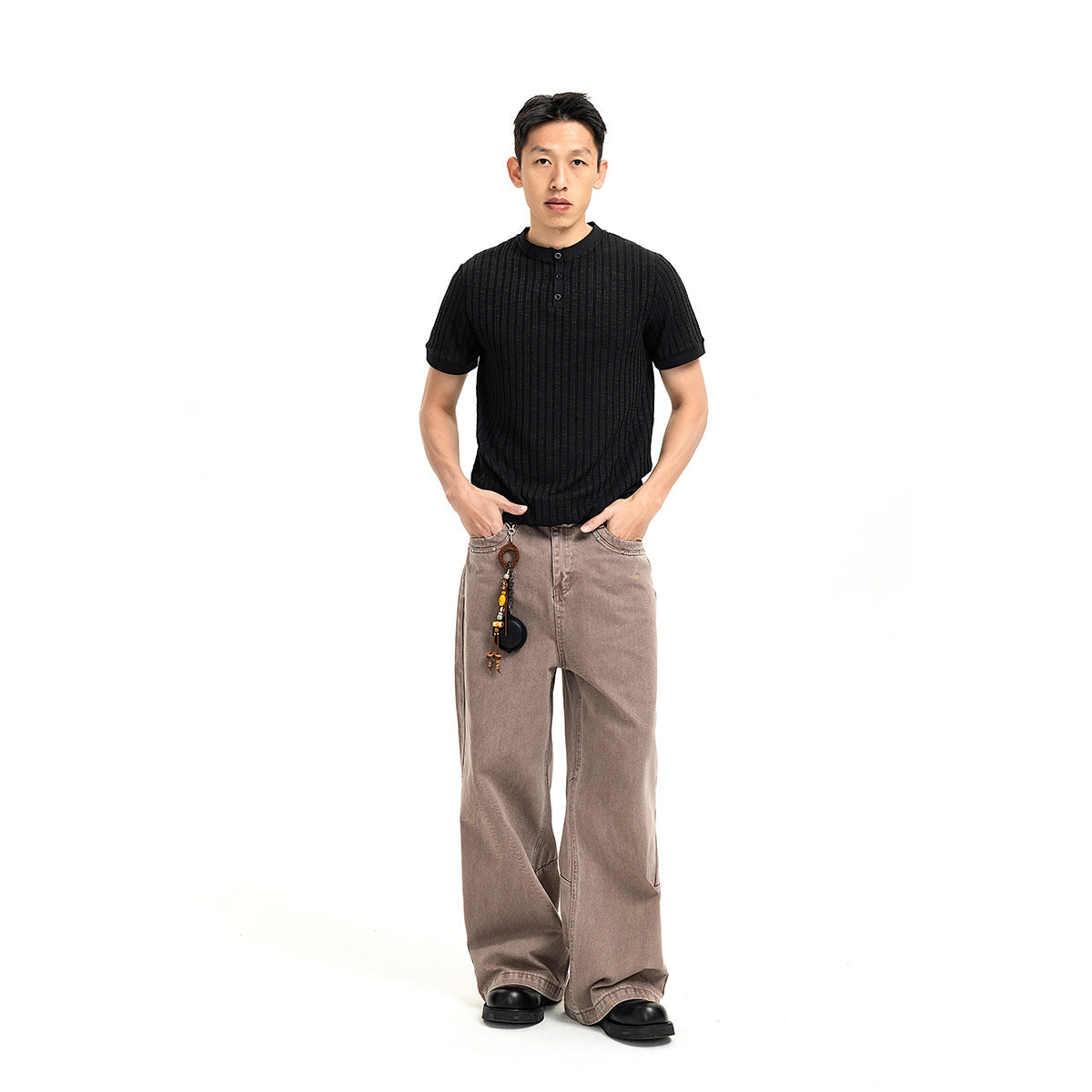 Full-length front view of a model wearing a black ribbed short-sleeve henley and loose taupe jeans.