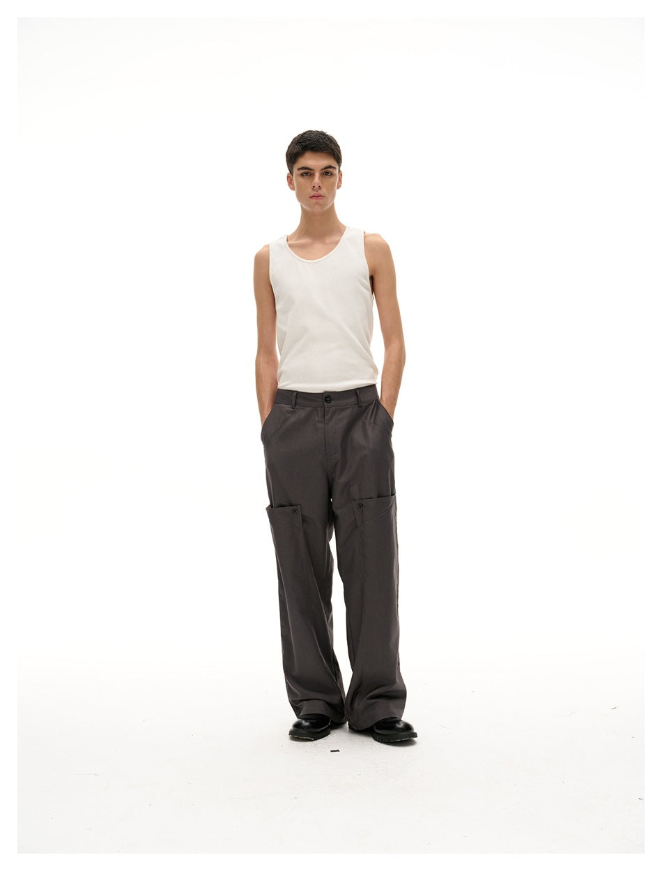 Model wearing dark gray wide-leg trousers with thigh flap pockets, a white tank top and black shoes, front view