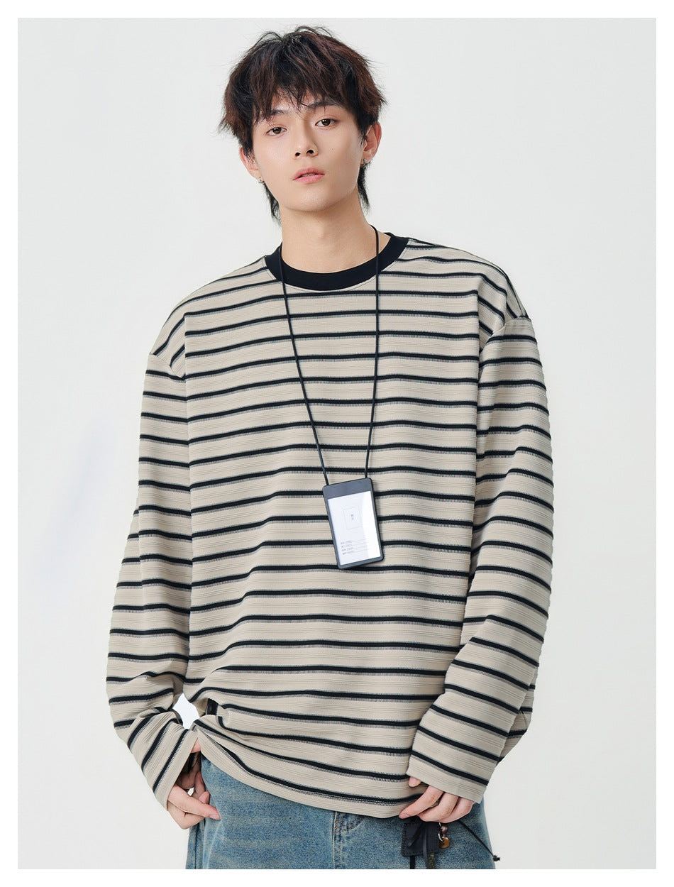 Model wearing an oversized beige long-sleeve shirt with thin black horizontal stripes and a black crew neck.