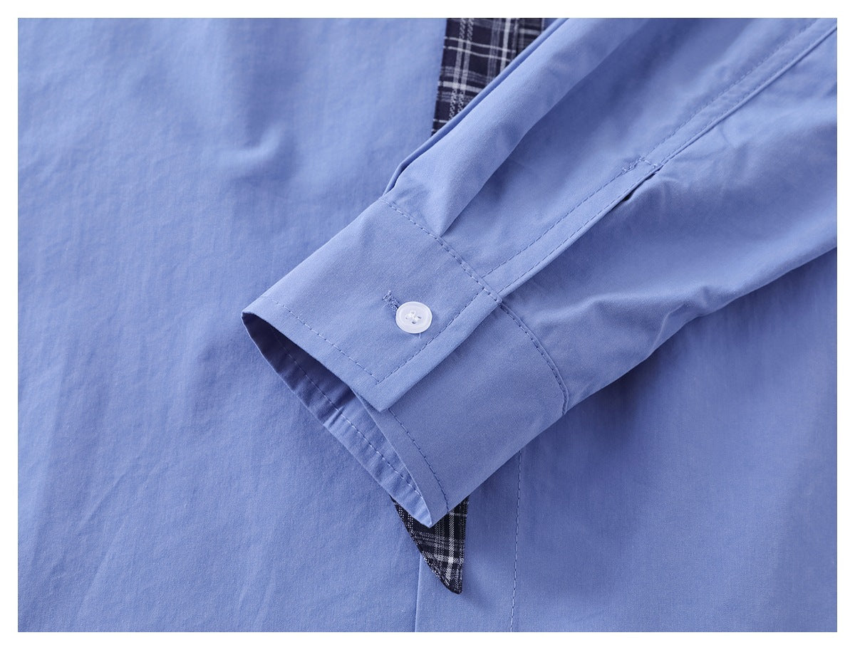 Close-up of a light blue shirt cuff with a white button and plaid fabric detail.