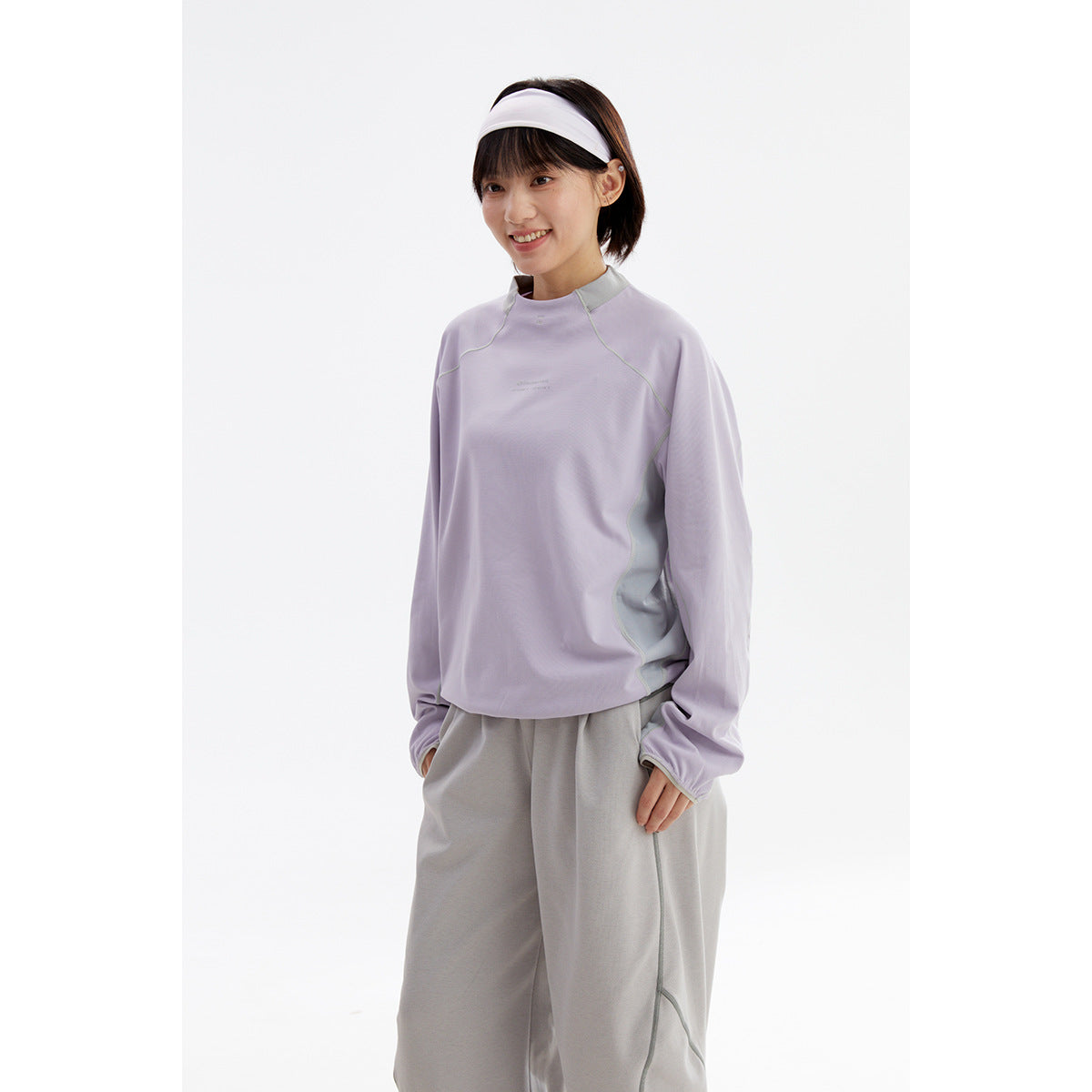 Woman wearing a lavender high-neck long-sleeve top with contrast seams and loose gray pants.