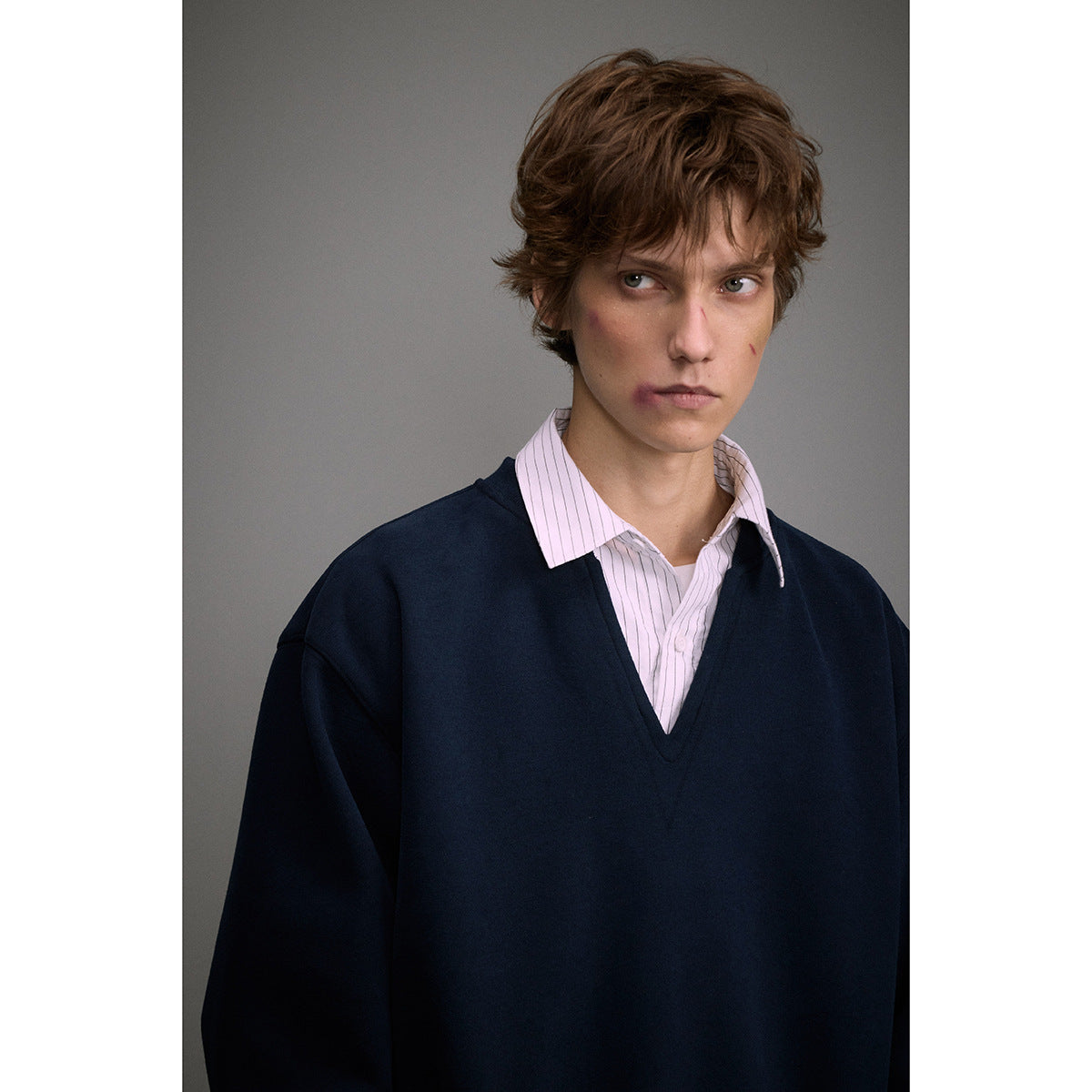 Close view of a model wearing a navy V-neck sweatshirt over a pale pink striped collared shirt.