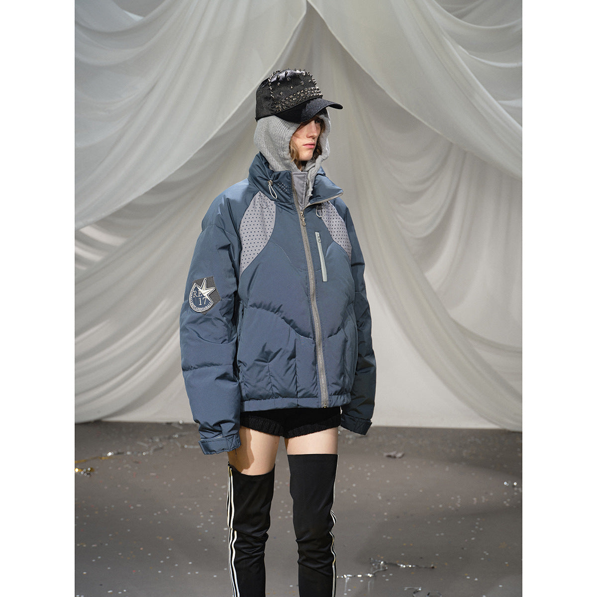 Closer view of a model wearing a blue-gray padded jacket with dotted shoulder panels and a star patch on the sleeve.