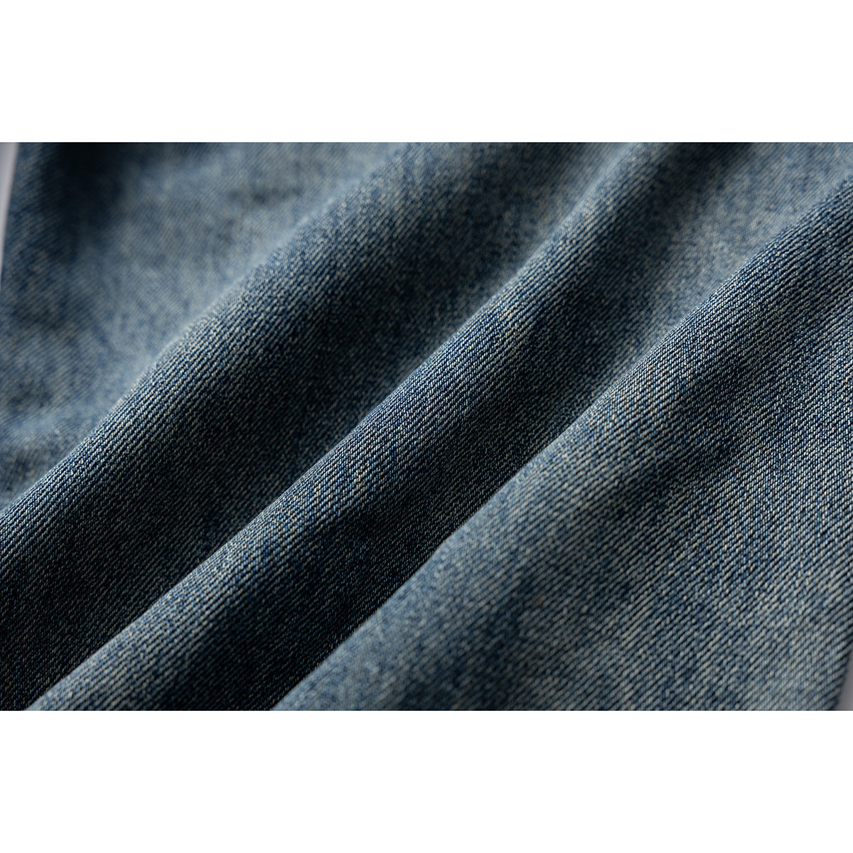 Macro view of blue denim fabric folded into ridges, showing its woven texture and varied wash.