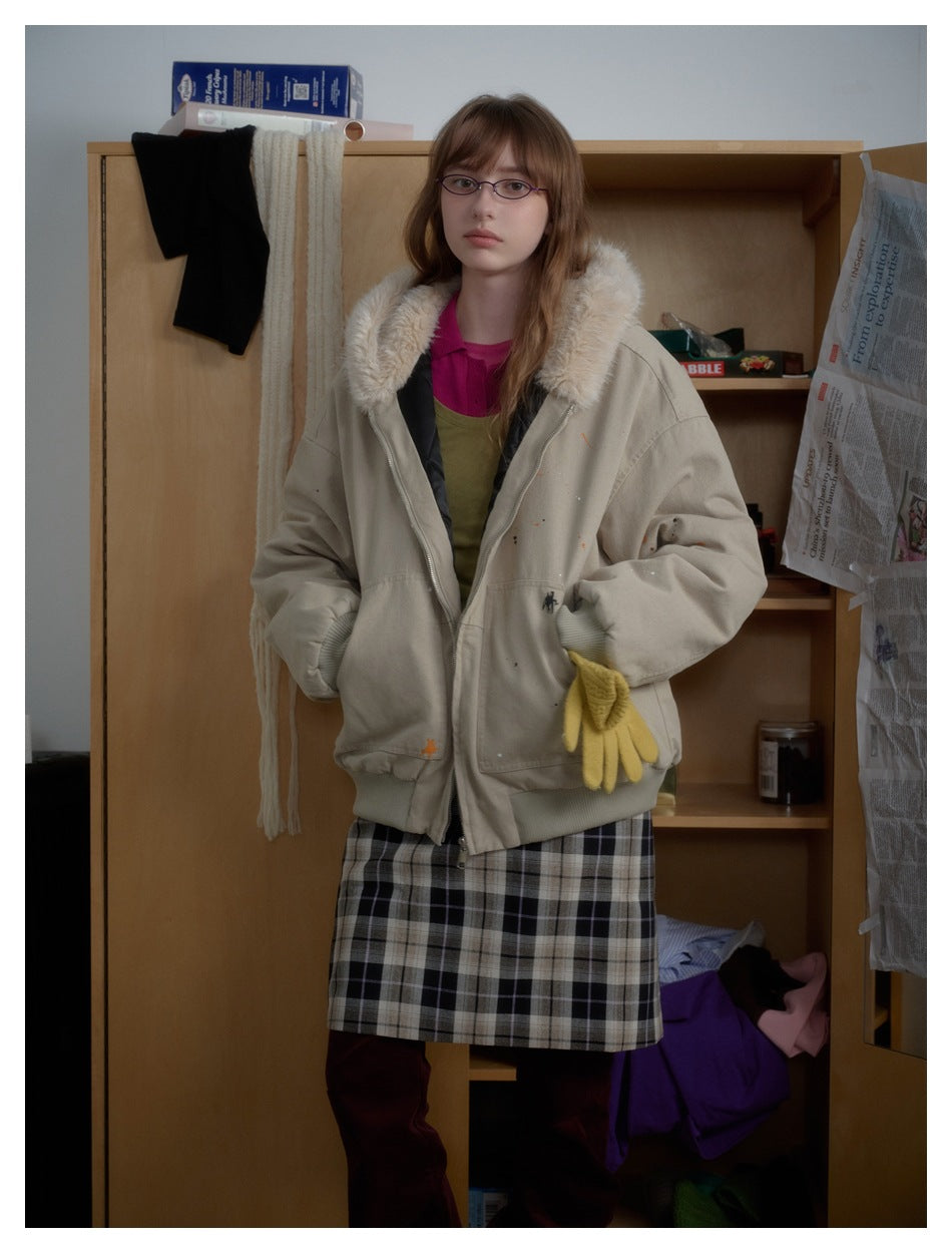 Model in a beige hooded zip jacket with fluffy hood trim, hands in pockets, with a plaid skirt and yellow glove