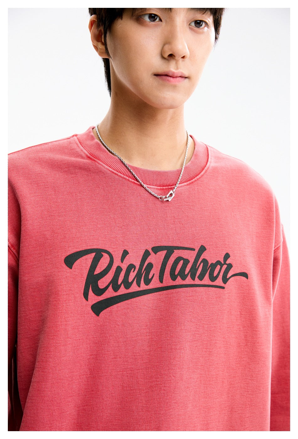 Close-up of a coral-pink crewneck sweatshirt showing its dark script chest print and ribbed neckline.