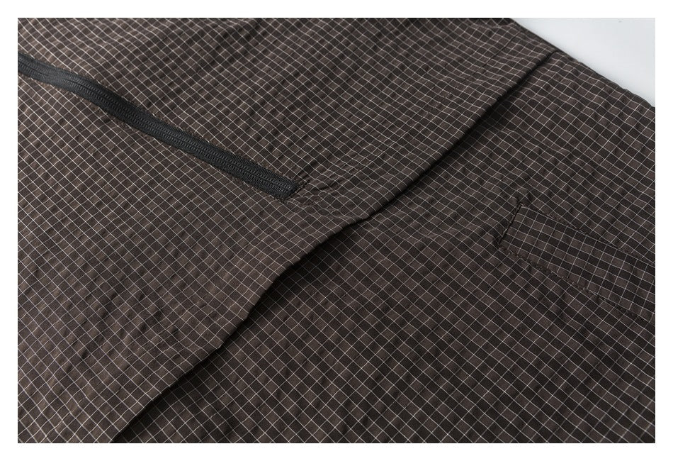 Close-up of dark brown checked garment showing a black zipper and curved pocket seam.