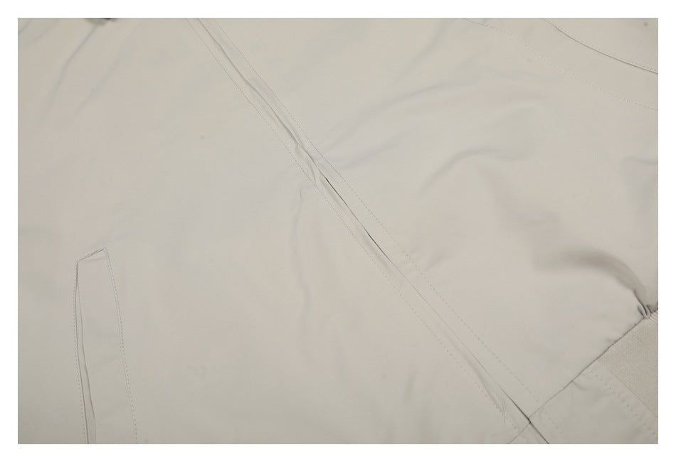 Close-up of ivory jacket fabric with stitched seams and part of a narrow welt pocket.