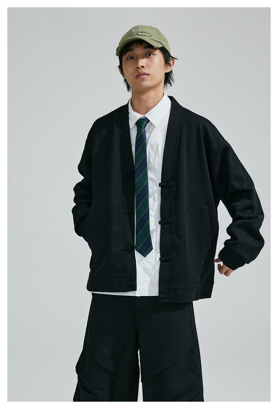 Model wearing a black frog-button cardigan with large front pockets over a white shirt and striped tie.