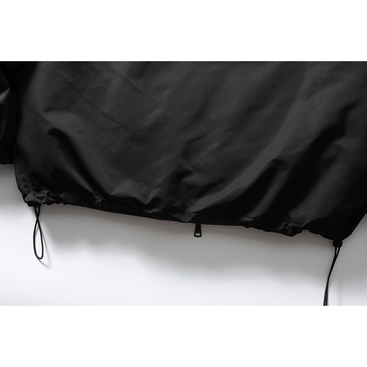 Close-up of the black jacket's gathered hem with adjustable drawcords and toggles.