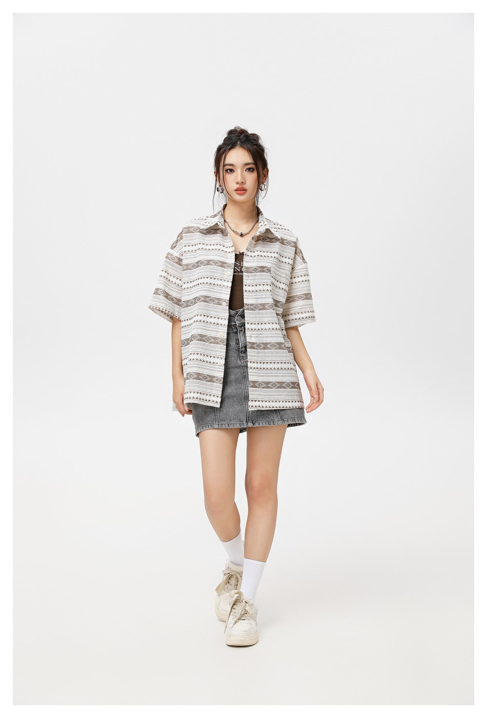Model wearing the brown striped short-sleeve shirt open over a brown top and gray denim skirt