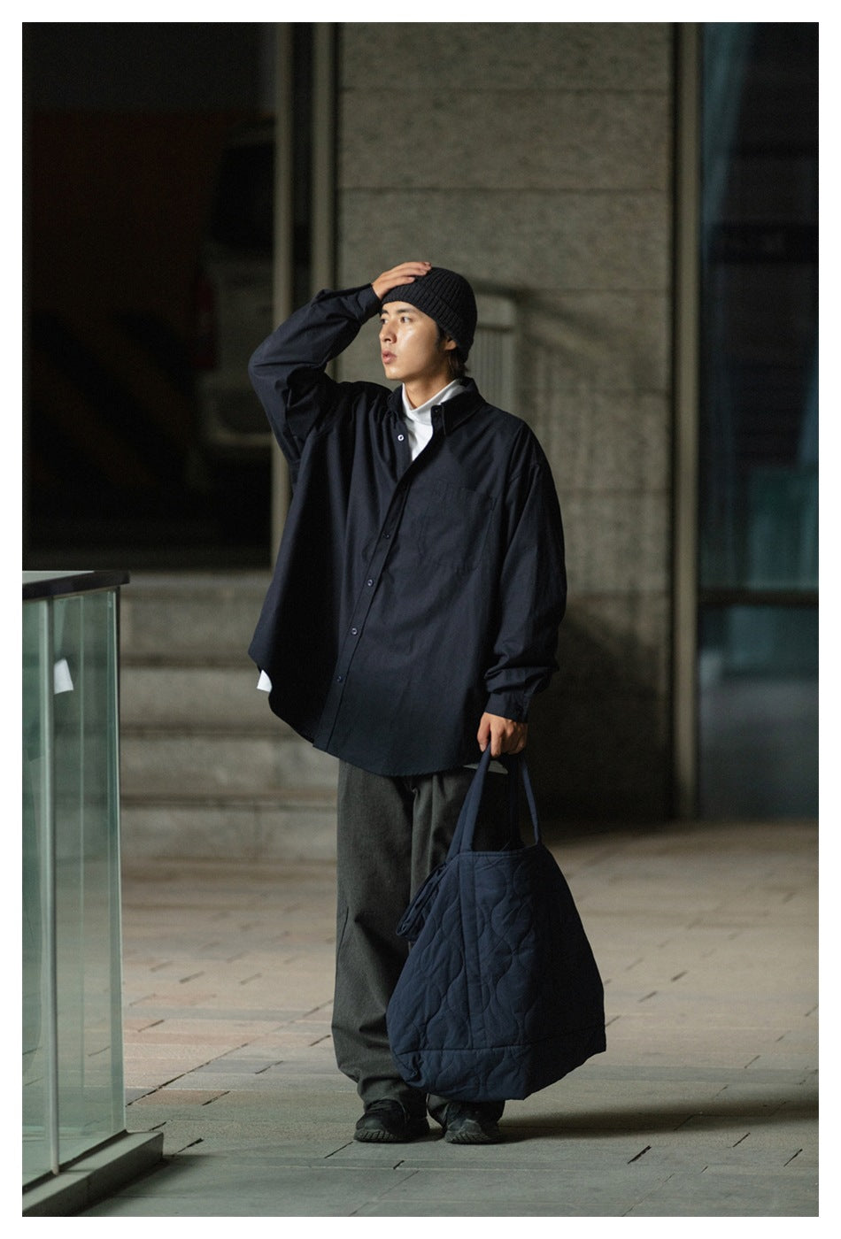 Model wearing an oversized black button-front shirt with a chest pocket, shown from the front with a black beanie.