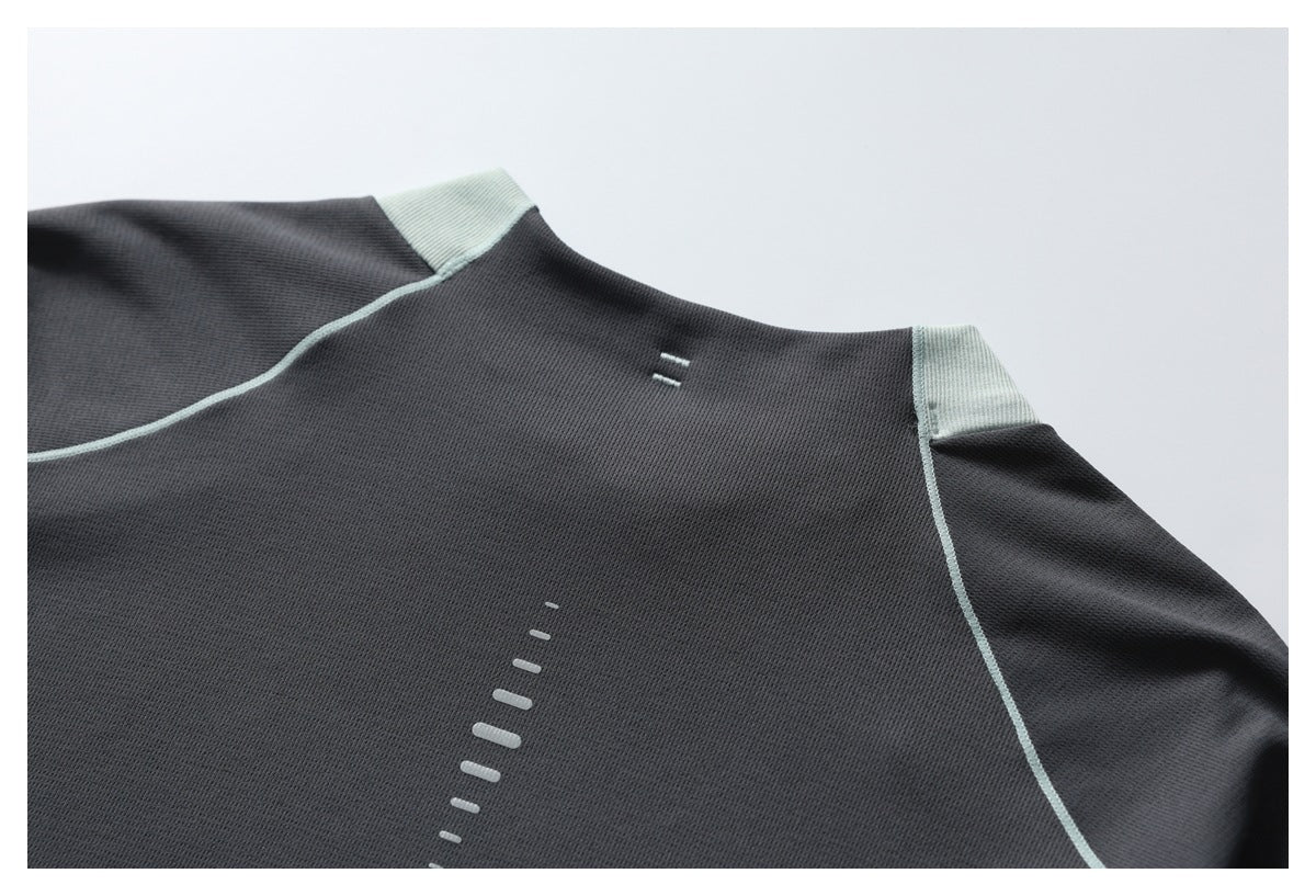 Close-up of a dark gray athletic top with pale mint seam piping and small reflective bar details.