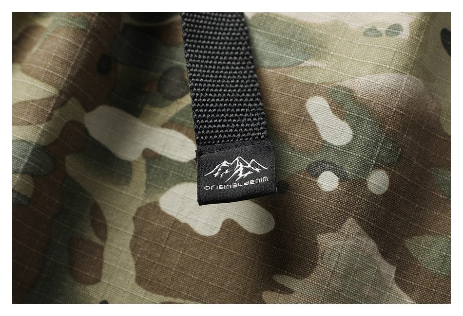 Close-up of a black woven label on green-brown camouflage fabric, with a white mountain logo and “original denim” text.