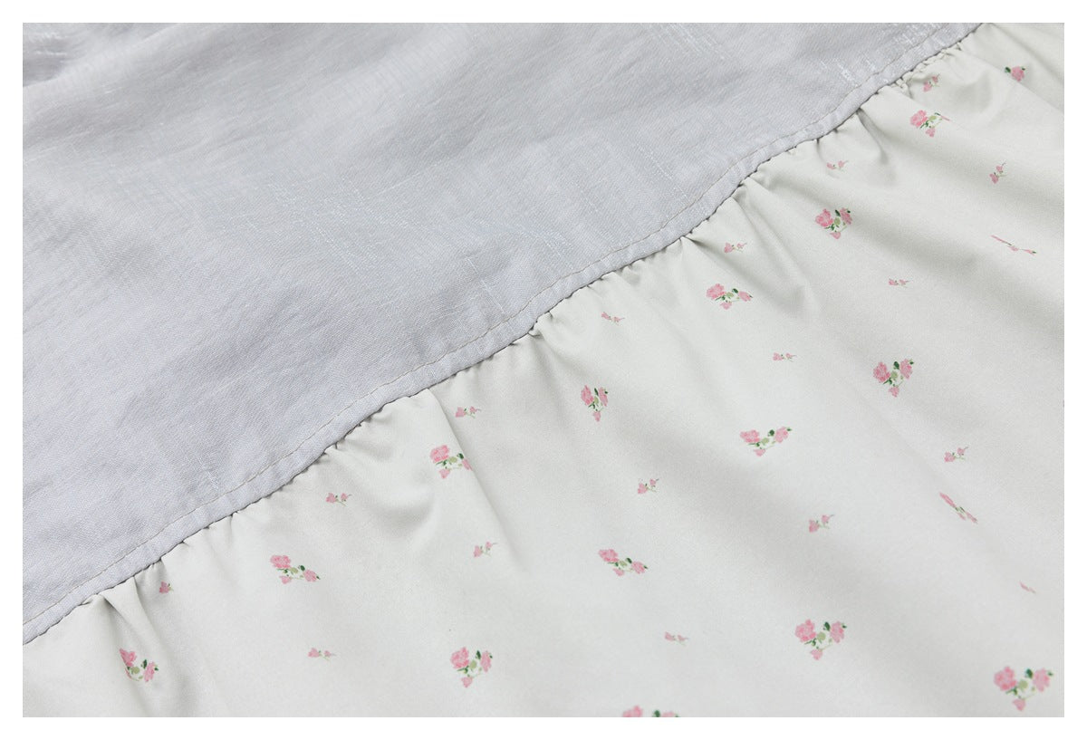 Close-up of white fabric with small pink floral prints joined by a gathered seam to pale gray fabric.