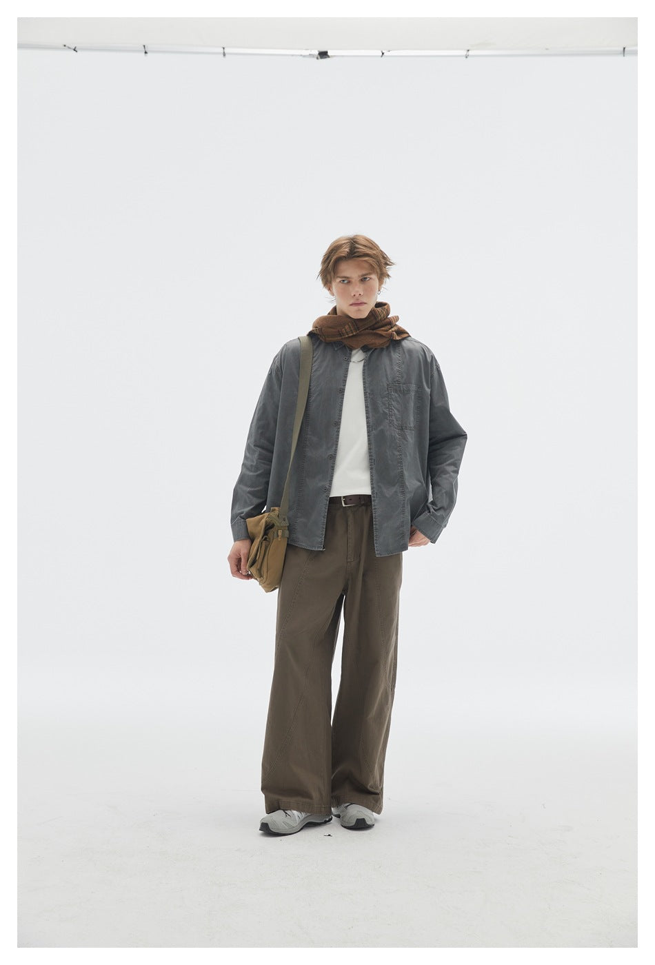 Model facing front wearing brown wide-leg pants with a gray shirt, white top, brown scarf and shoulder bag