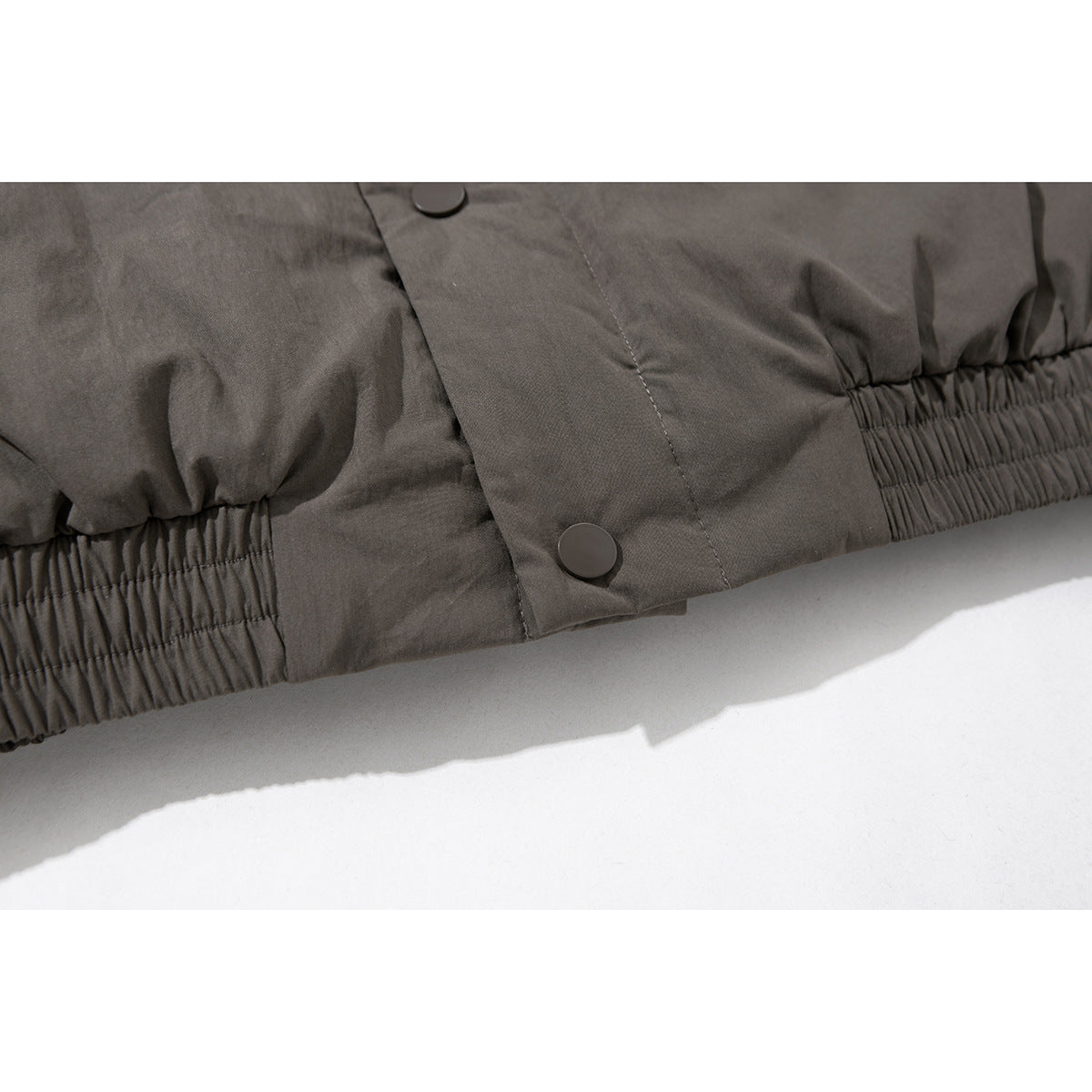 Close-up of the charcoal gray jacket's gathered elastic hem and snap-button front placket.