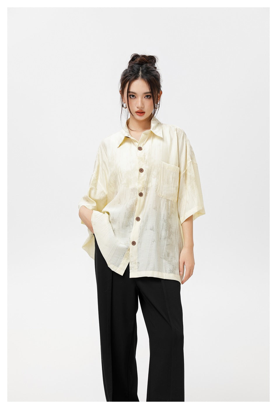 Model wearing an oversized ivory button-up shirt with brown buttons and a chest pocket, paired with black trousers.