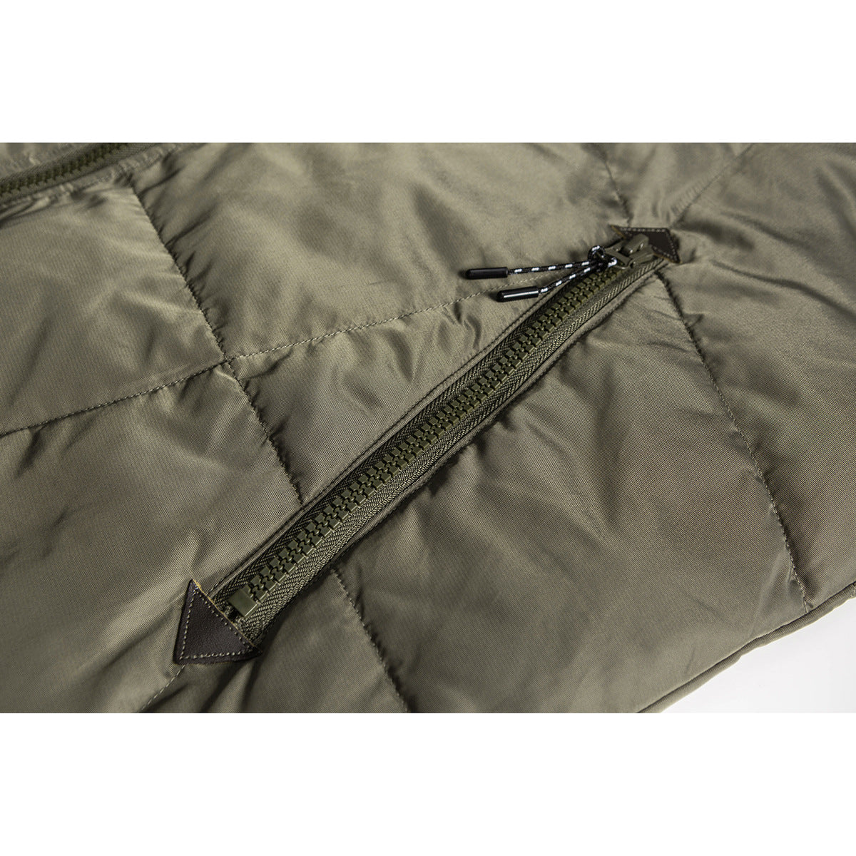 Close-up of an olive quilted jacket pocket with a diagonal zipper and corded pulls.