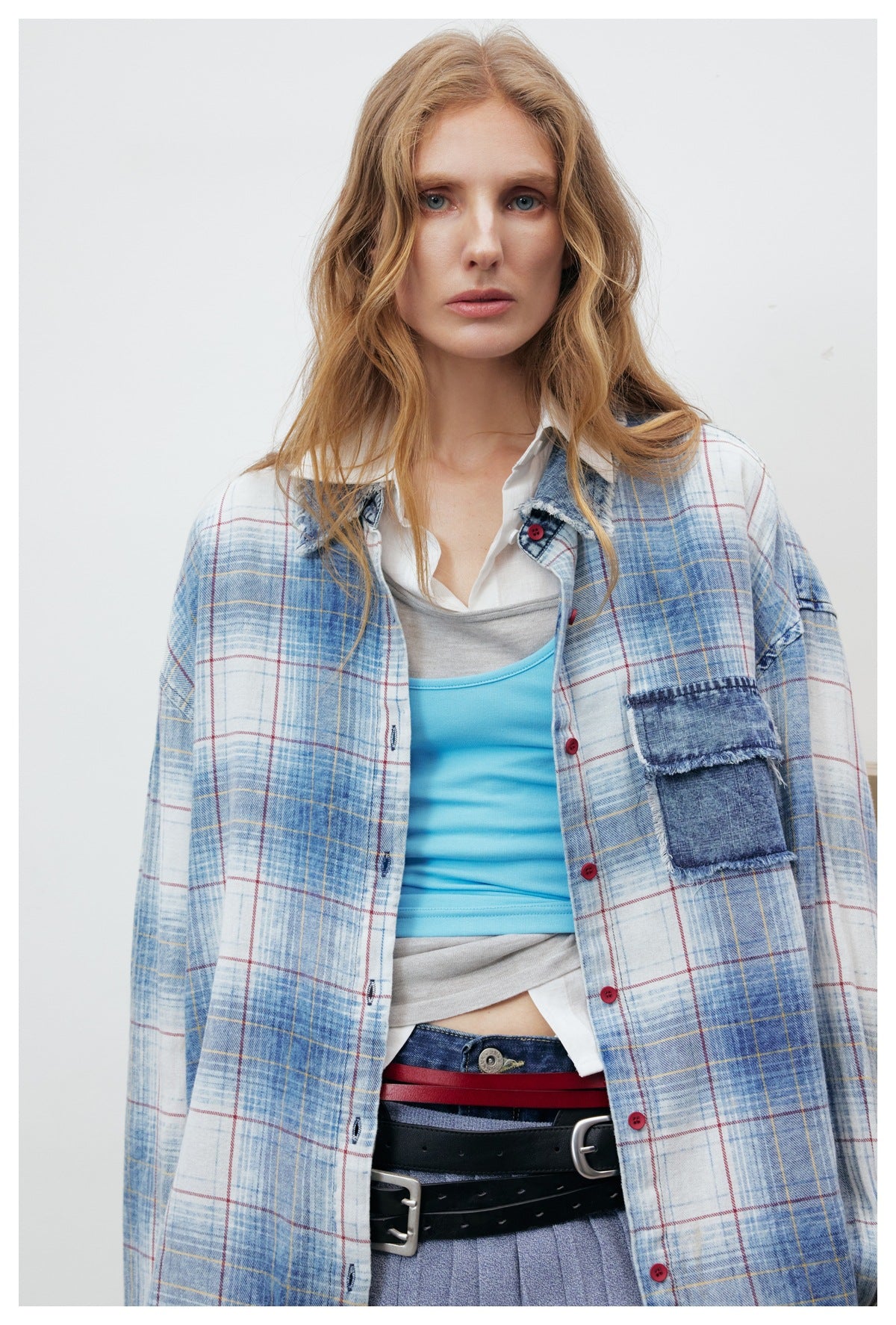 Close view of a model wearing a blue-and-white plaid shirt with a frayed denim chest pocket and red buttons.