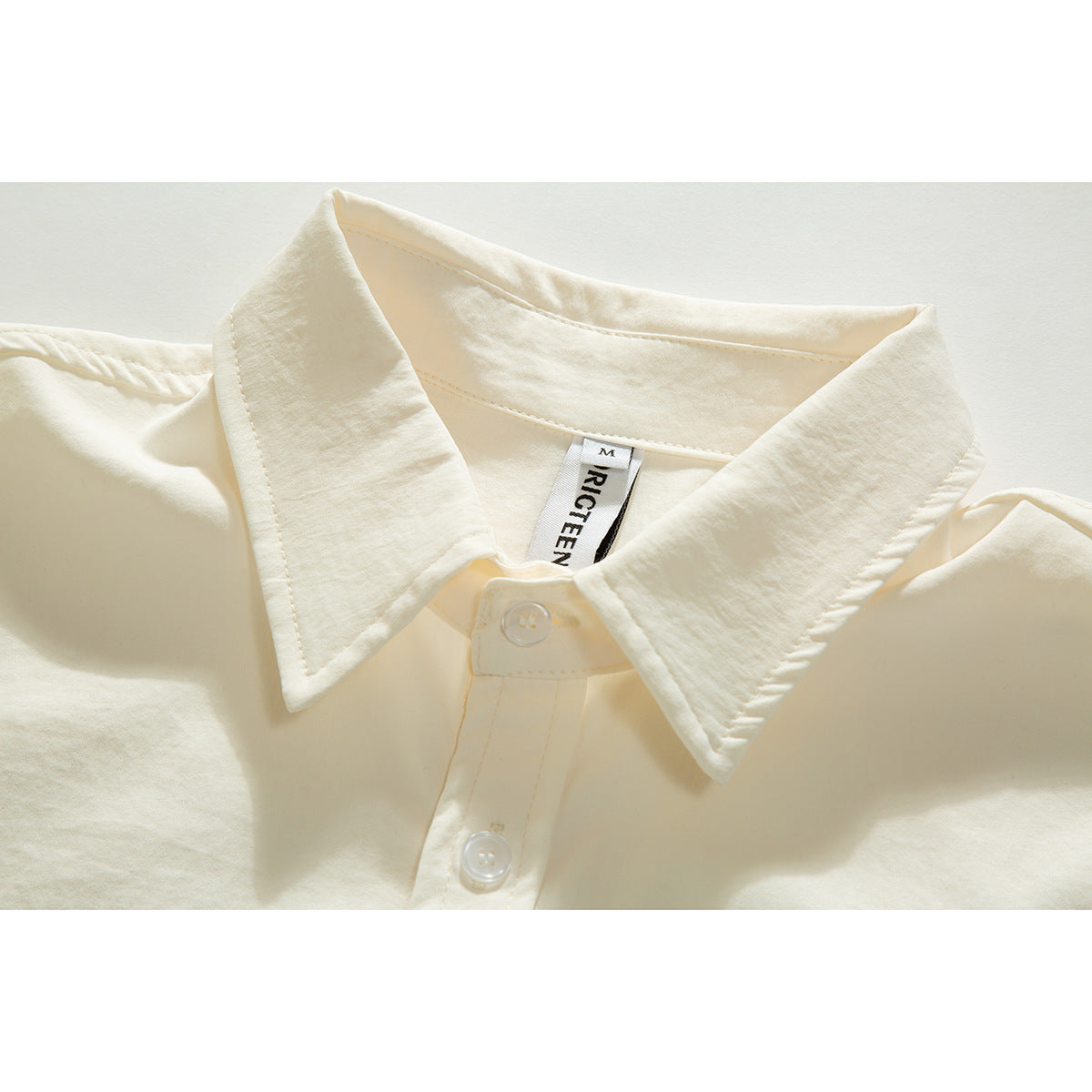 Close-up of an ivory shirt's oversized pointed collar, top buttons, and sewn neck label.