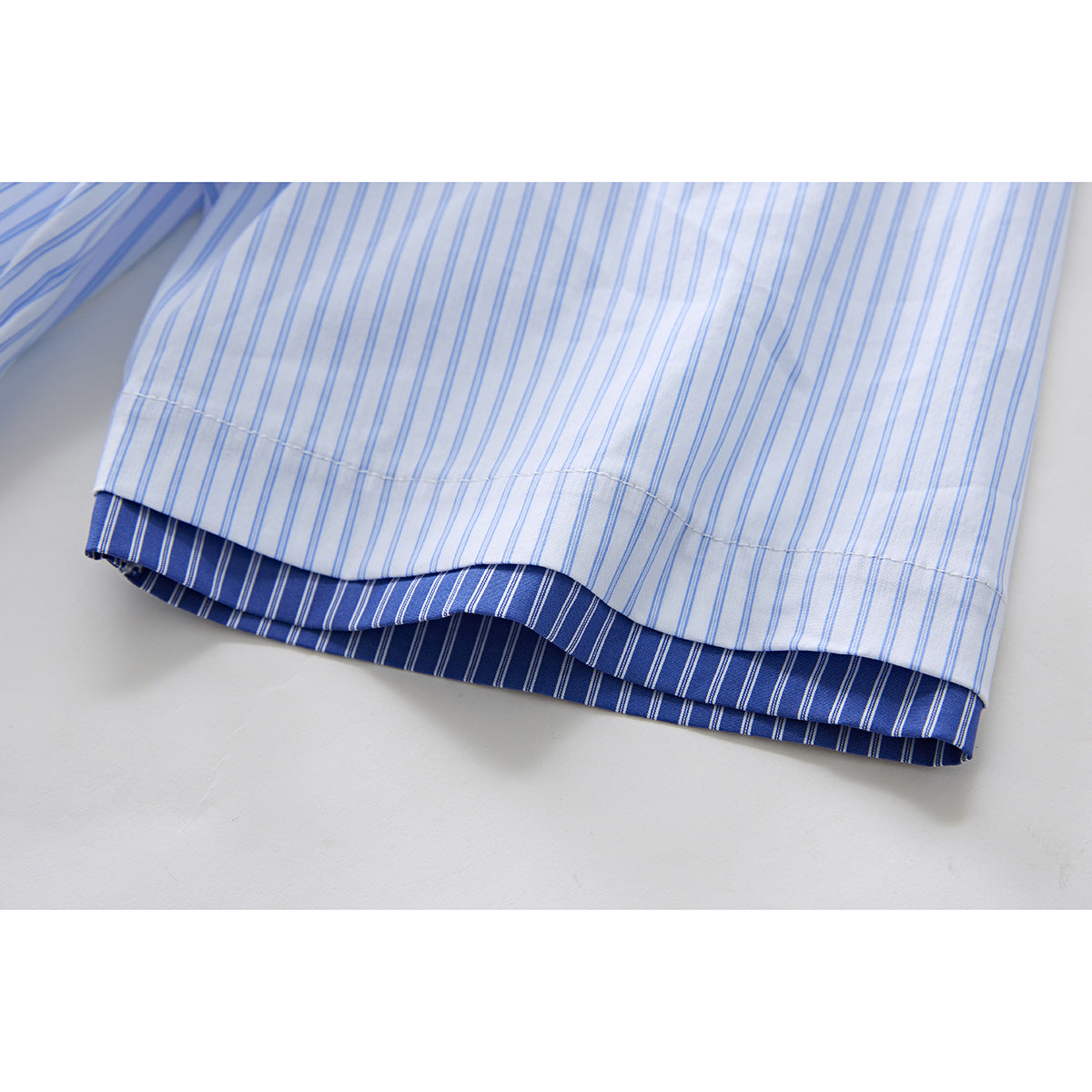 Close-up of the hem showing the white shirt's fine blue stripes and dark blue striped inner trim.