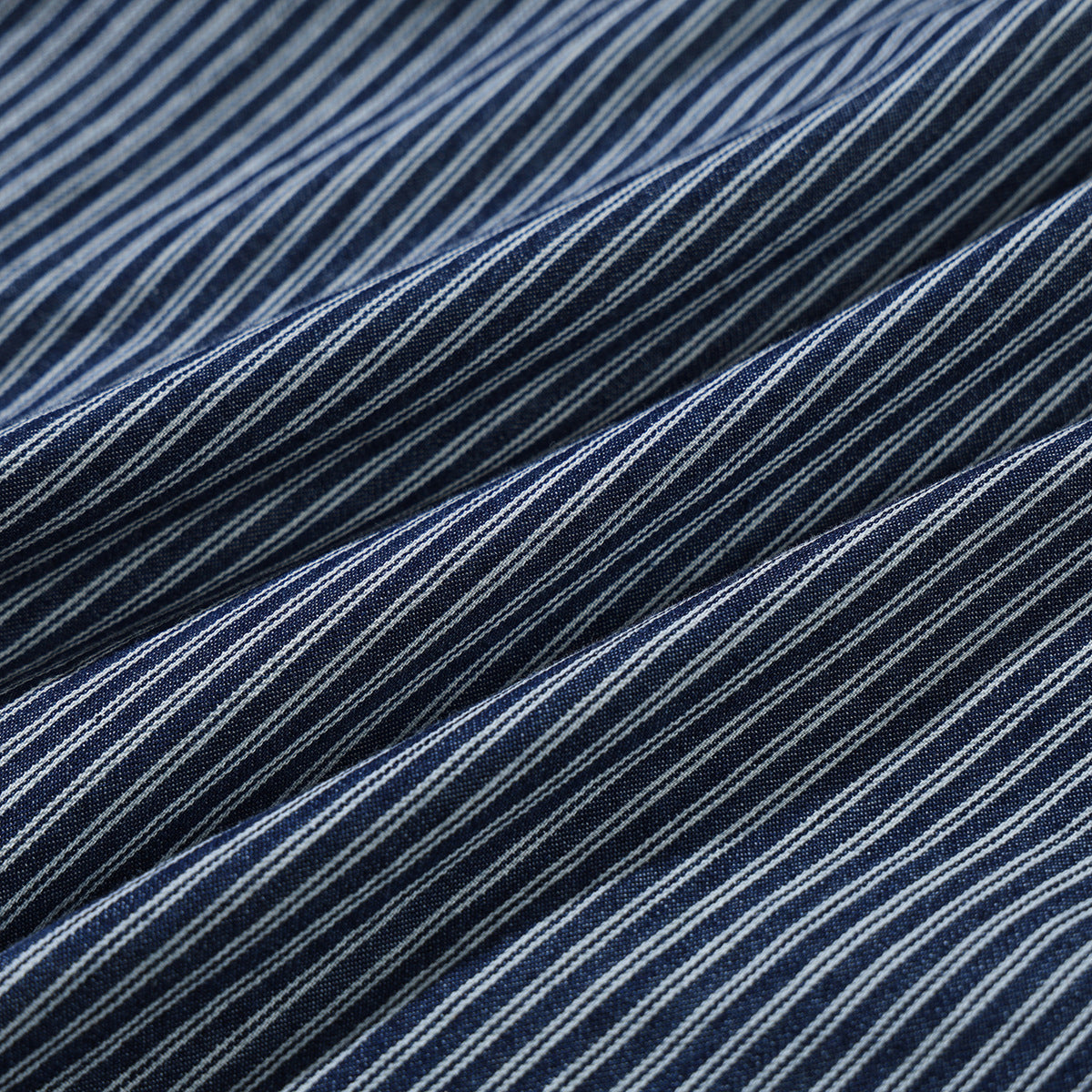Macro view of folded dark blue fabric with narrow white stripes.