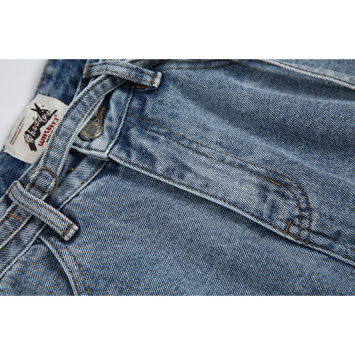 Close-up of light blue jeans with a button, belt loop, front pocket stitching and a sewn waistband label.