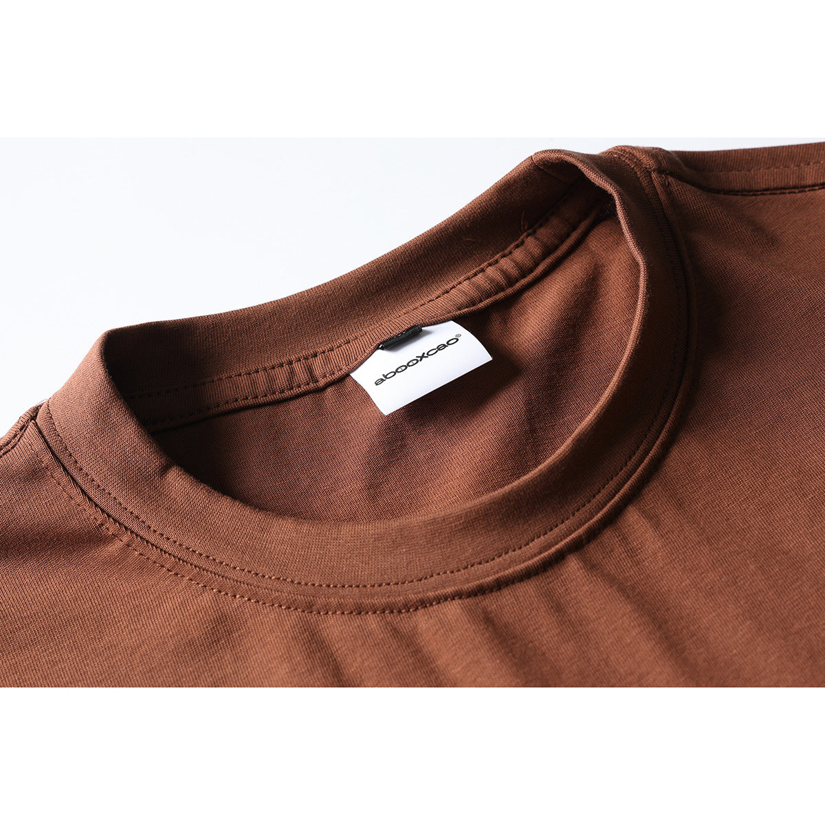 Close-up of a rust-brown T-shirt neckline with ribbed collar stitching and a white inner brand label.