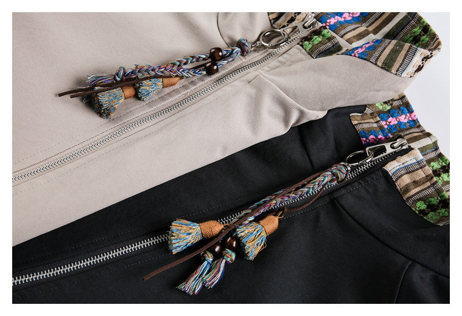 Close-up of beige and black jacket zippers with braided multicolor tassel pulls and patterned collar trim.