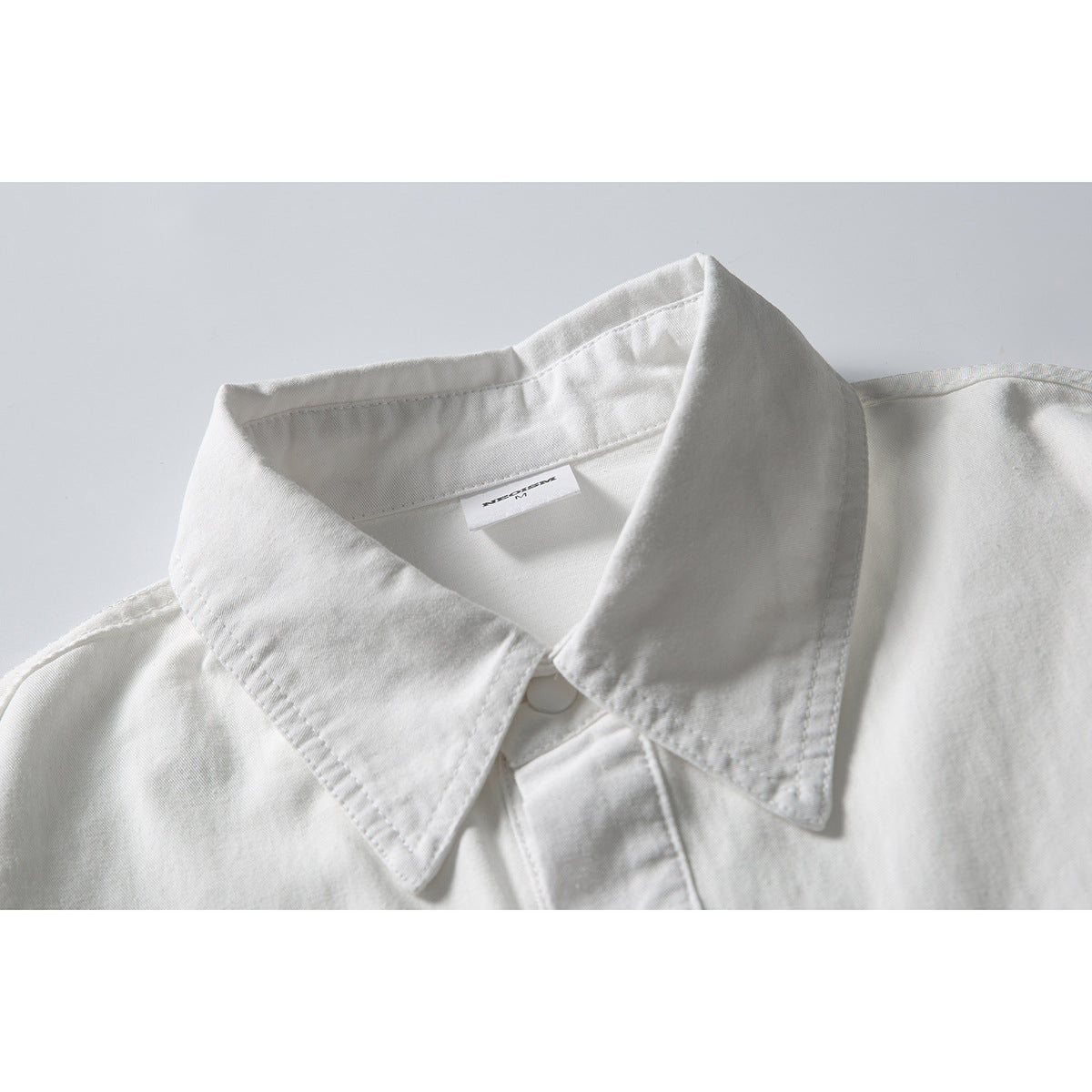 Close-up of a white shirt's pointed collar, button placket, and inner neck label.