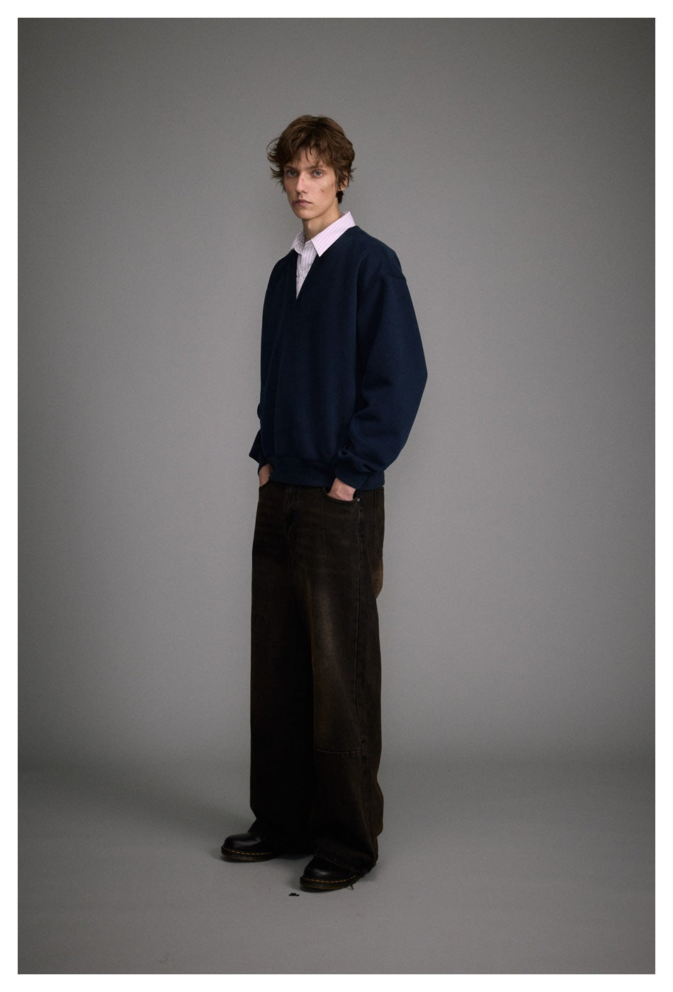 Full-length view of model in navy V-neck sweatshirt with striped collar, wide dark pants and black boots