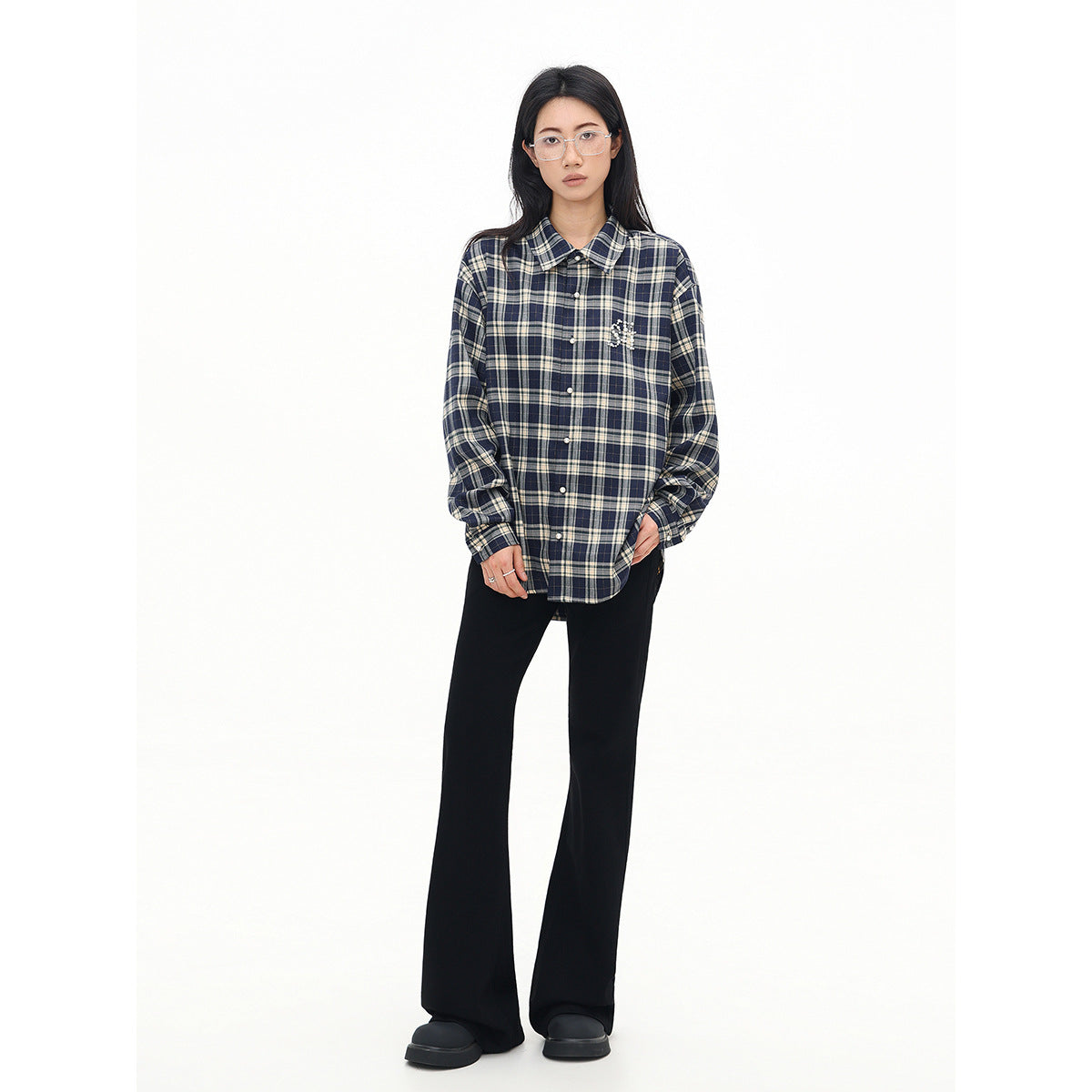 Model wearing a buttoned navy and cream plaid shirt with a beaded chest embellishment and black flared pants.