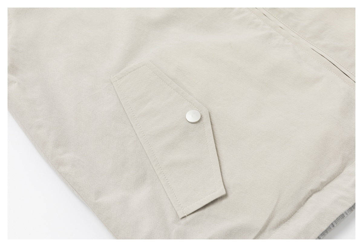 Close-up of a beige jacket's angular flap pocket with a round silver snap.