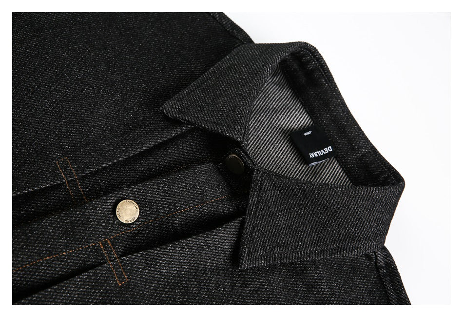 Close-up of a black jacket collar, inner label, brass-tone button, and orange stitching.