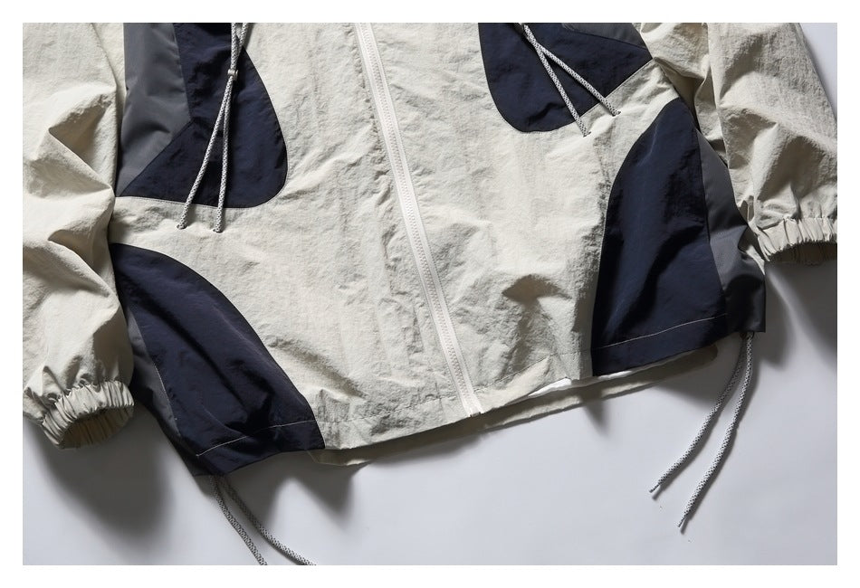 Lower front of an off-white jacket showing navy panels, elastic cuffs, dangling cords, and a white zipper.