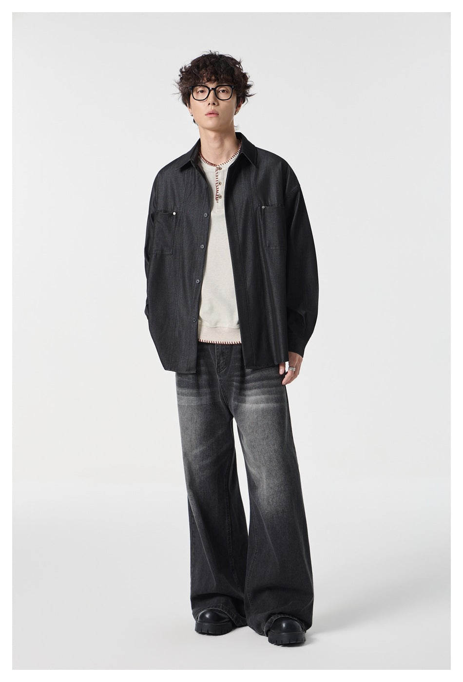 Full-length model wearing a dark charcoal button-up shirt with two chest pockets over a cream top and faded wide-leg jeans.