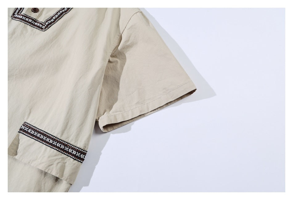 Beige short-sleeve shirt detail showing the sleeve, trimmed cuff, and part of the embroidered placket.