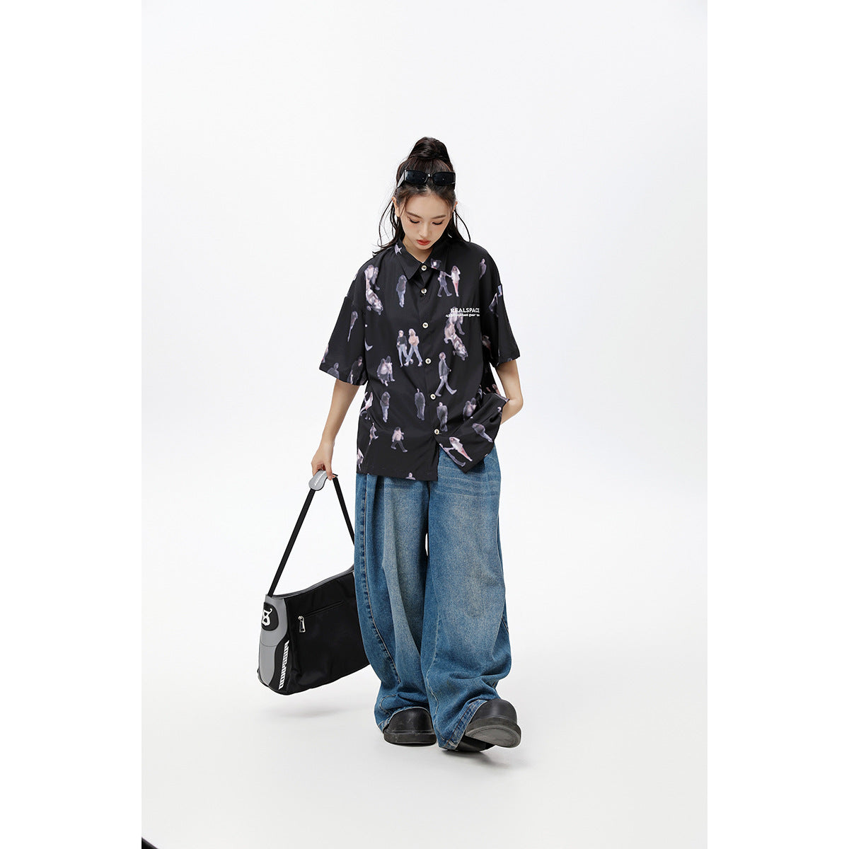 Model wearing a loose black short-sleeve button-up shirt with a light figure print and white chest lettering.