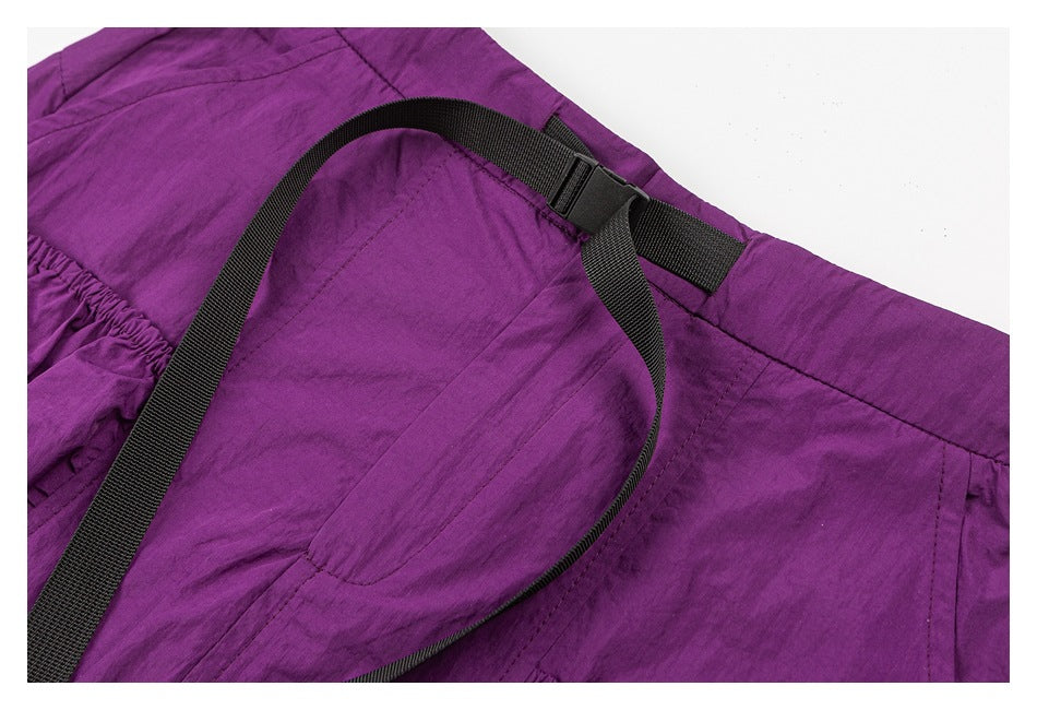 Close-up of purple pants showing a black webbing belt and buckle at the waistband.