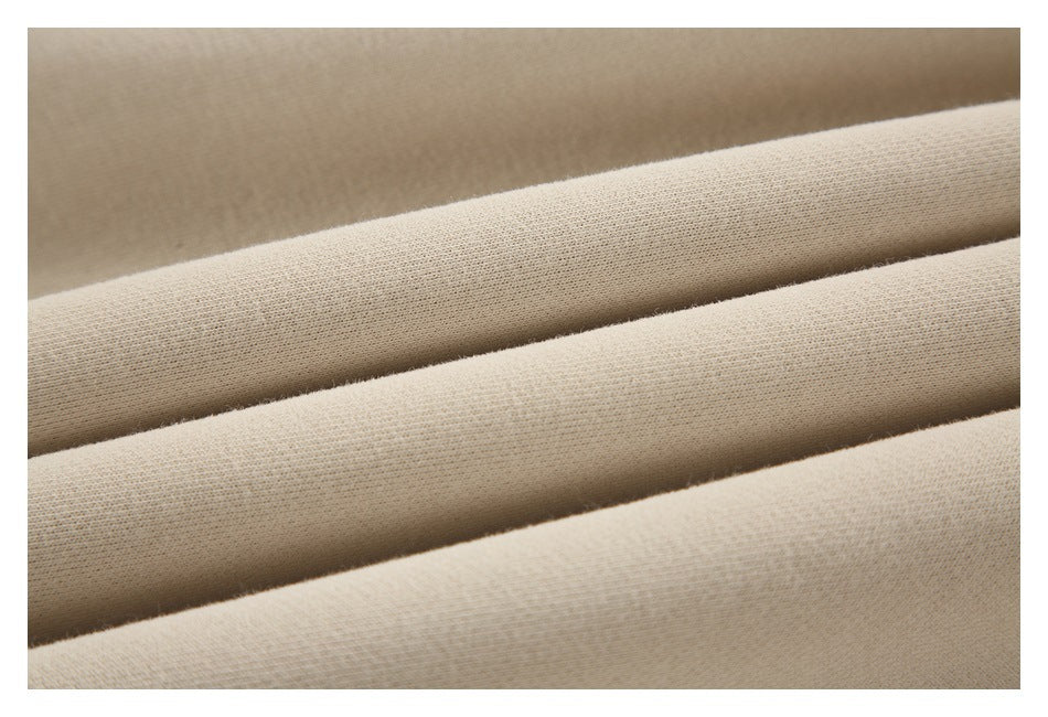 Close-up of beige sweatshirt fabric arranged in soft folds, showing its surface texture.