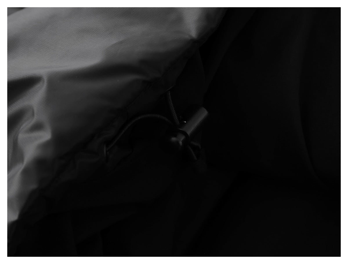 Dark close-up of a black jacket's hem with an elastic drawcord and toggle.
