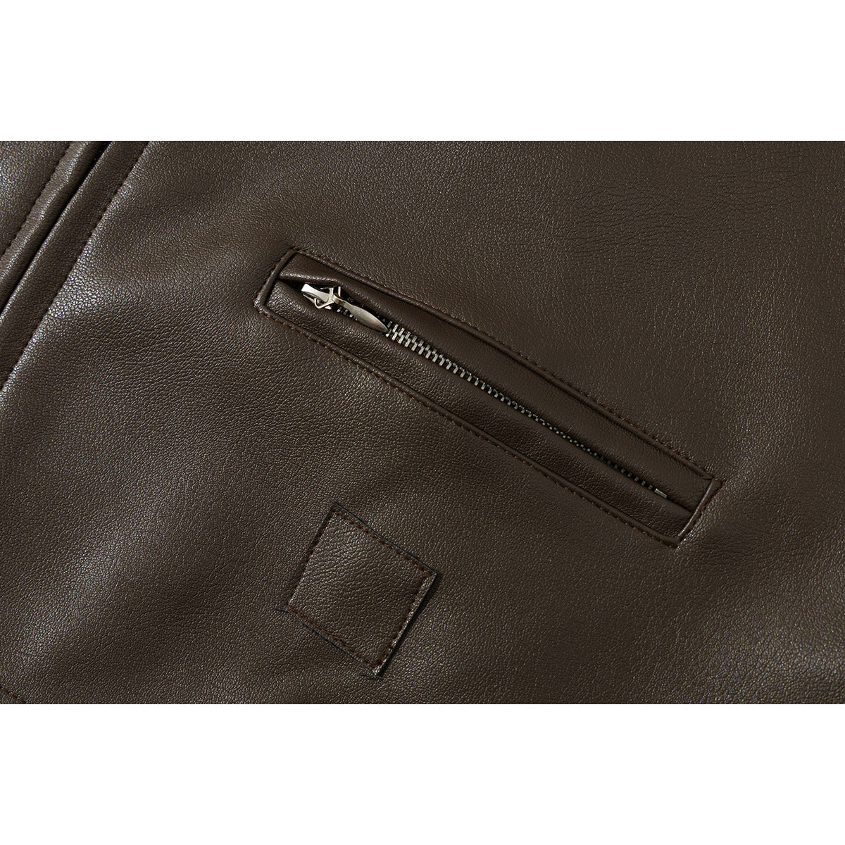 Close-up of a dark brown jacket’s diagonal zippered chest pocket and a small stitched patch.