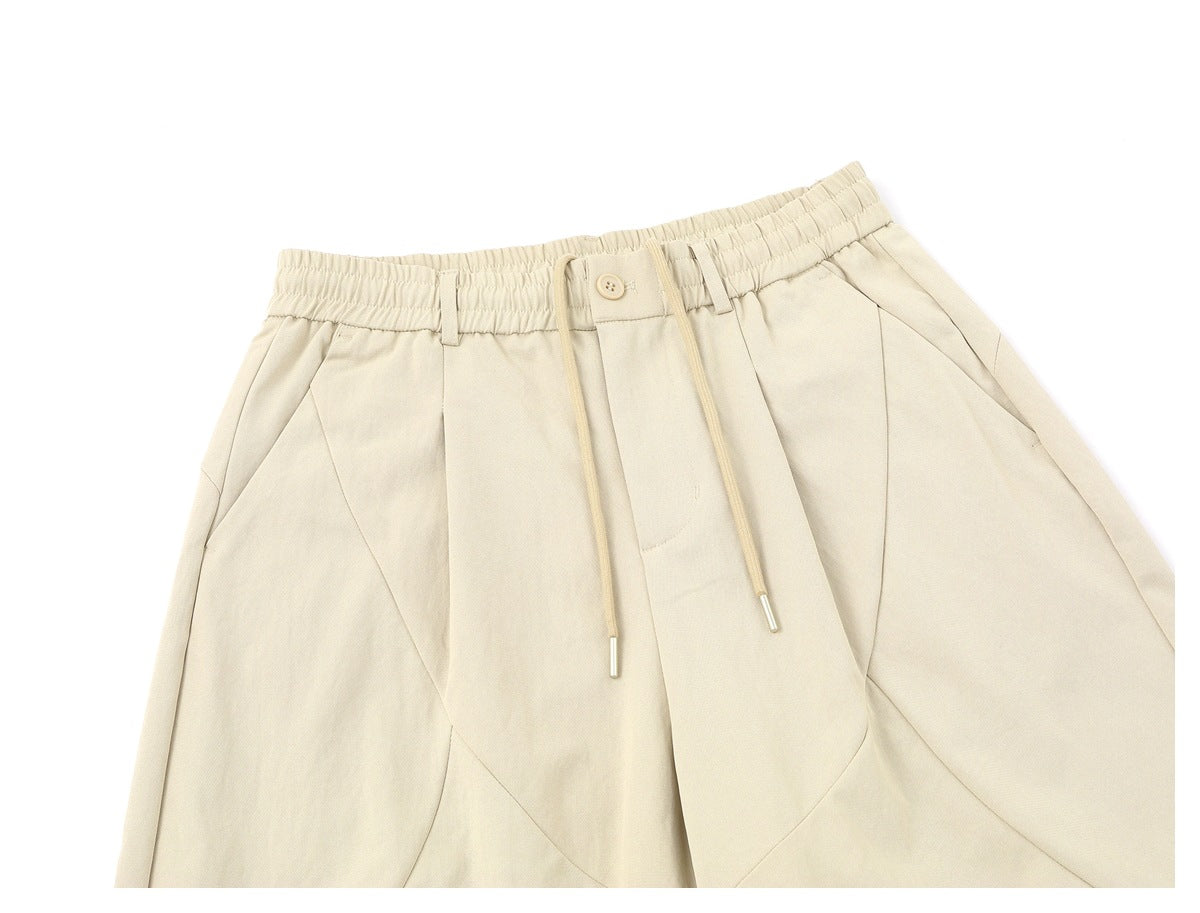 Close-up of the cream trousers' elasticated waistband, button closure, drawstrings, belt loops and curved front seams.
