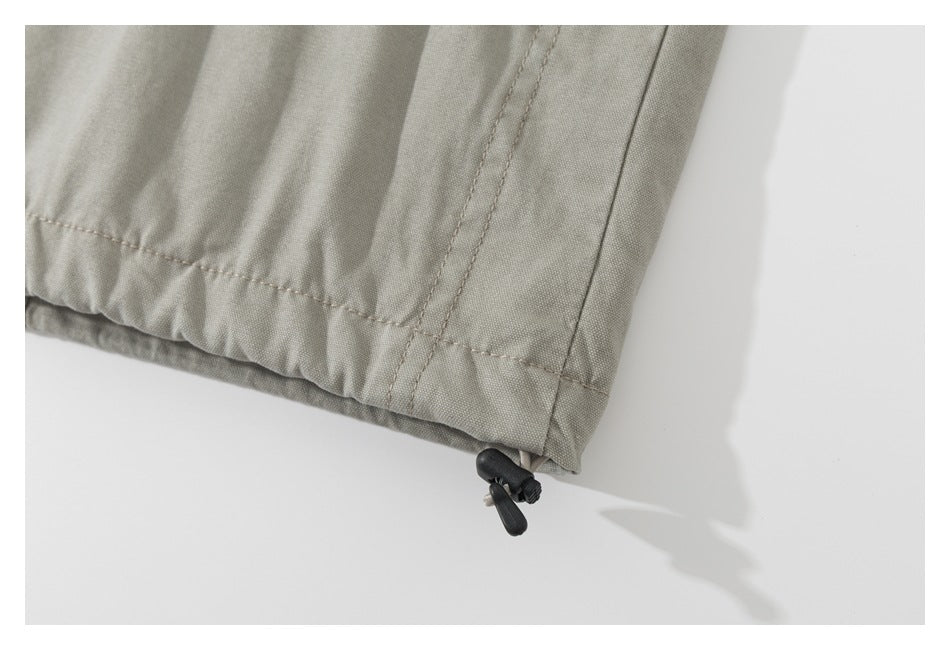 Close-up of the light khaki jacket hem with a black adjustable drawcord toggle.