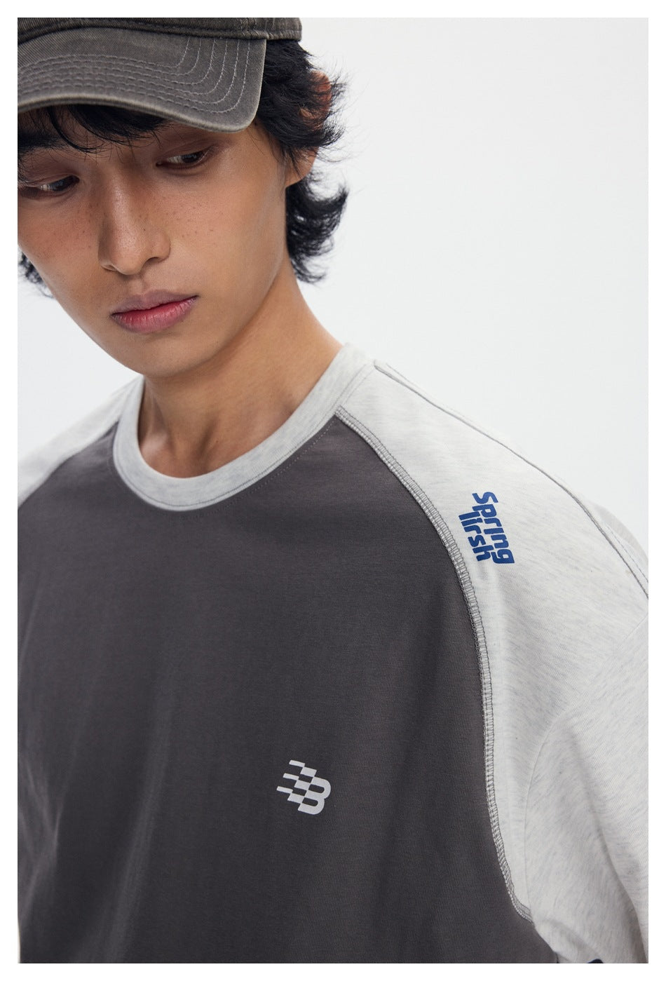 Close-up of the T-shirt's charcoal body, light gray raglan sleeve, contrast stitching, and small chest emblem.