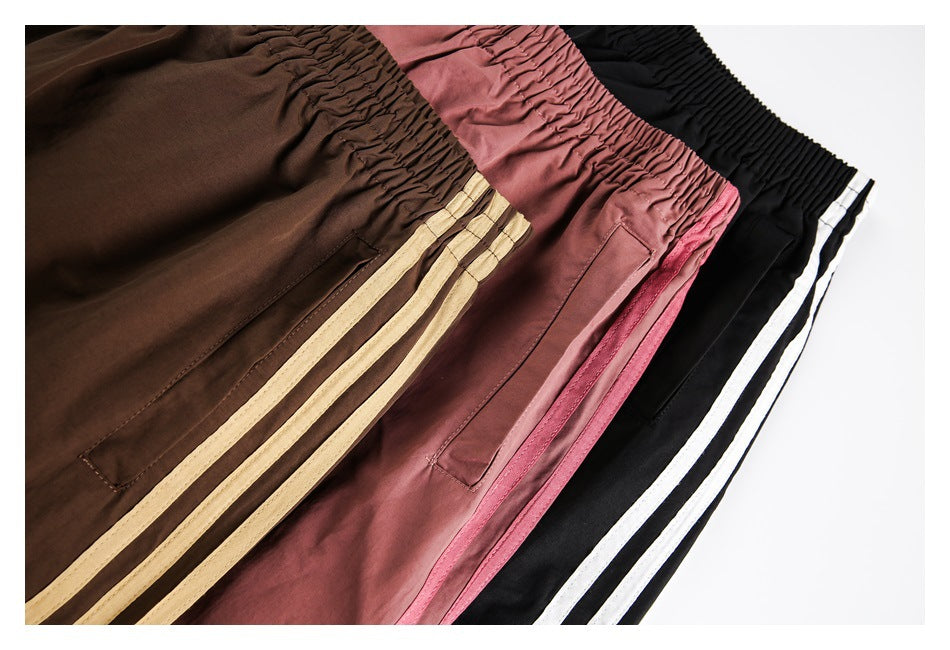 Brown, dusty rose, and black track pants laid side by side, each with an elastic waist and contrasting side stripes.