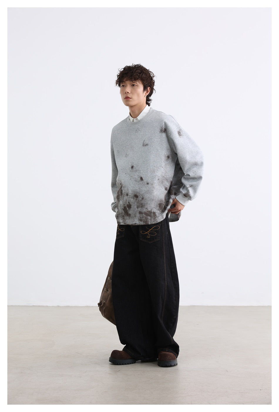 Model wearing a light gray crewneck sweatshirt with dark distressed splashes concentrated near the hem.